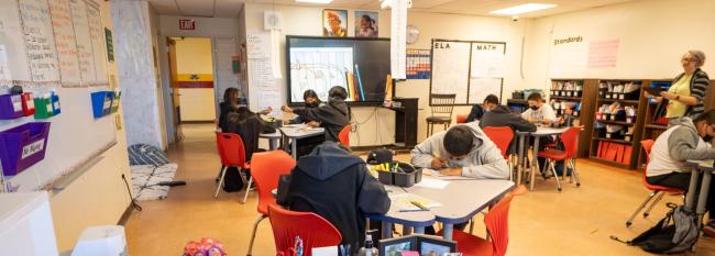 A classroom filled with students seated at desks and chairs, engaged in learning activities.