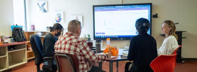 A group of school staff members seated around a table, engaged in discussion in front of a large presentation screen.