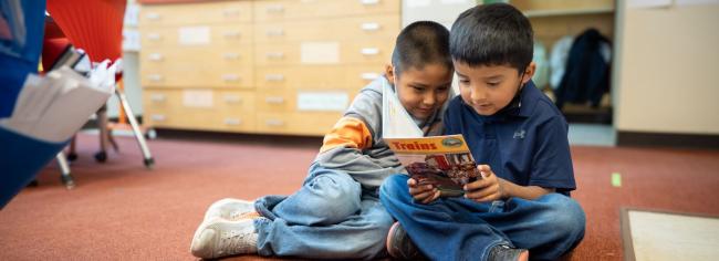 Two students sitting on the floor and reading together.