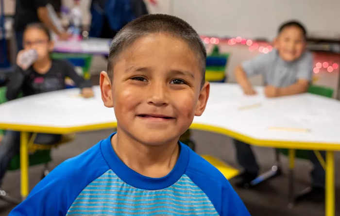 Young boy smiling at the camera in a classroom.